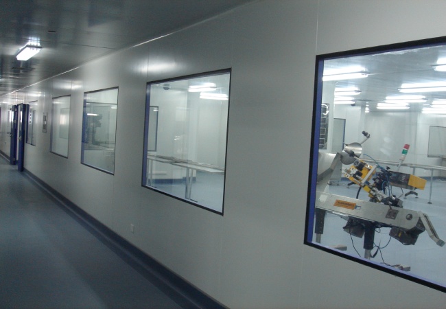Pharma cleanroom support corridor with observation windows and sample preparation equipment behind modular wall panels
